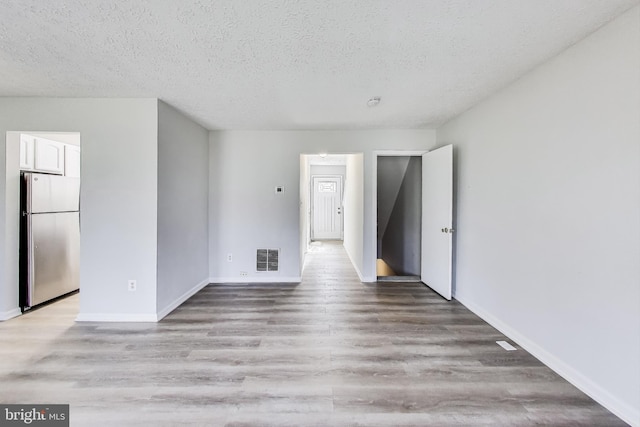 unfurnished room with visible vents, a textured ceiling, light wood-type flooring, and baseboards