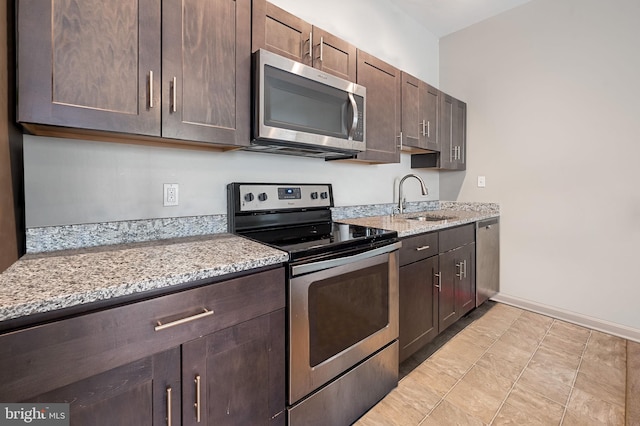 kitchen with dark brown cabinetry, stainless steel appliances, light stone counters, and a sink