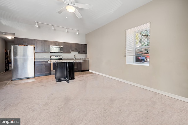 kitchen with light carpet, a sink, a center island, appliances with stainless steel finishes, and baseboards