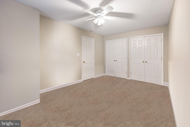 unfurnished bedroom with baseboards, two closets, ceiling fan, and carpet