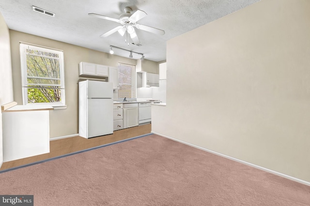 interior space featuring visible vents, freestanding refrigerator, rail lighting, a textured ceiling, and light carpet