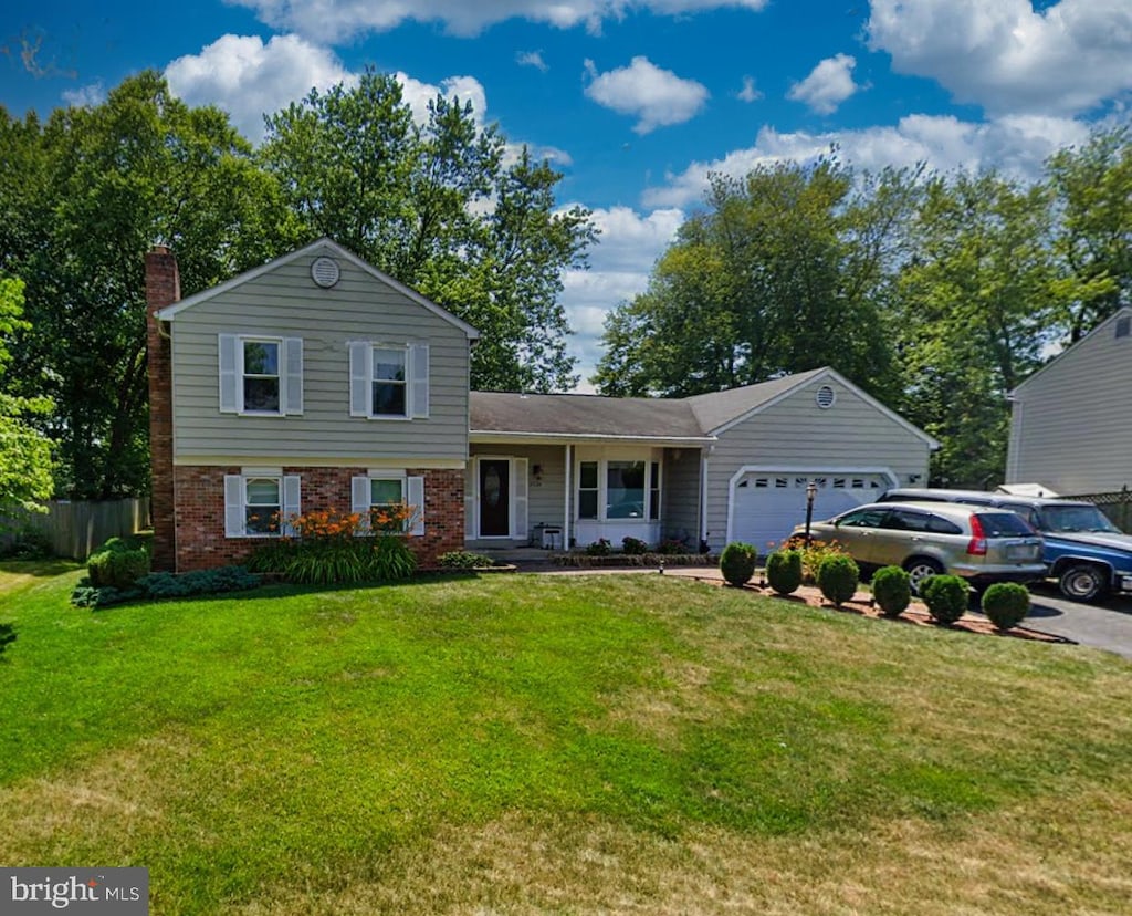 tri-level home with a front yard, driveway, a chimney, a garage, and brick siding