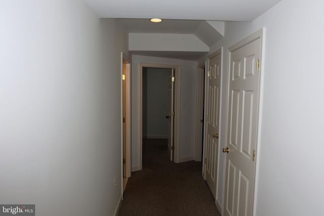 hall featuring dark carpet and baseboards