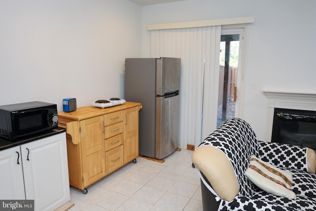 kitchen featuring light tile patterned flooring, a fireplace, freestanding refrigerator, and black microwave