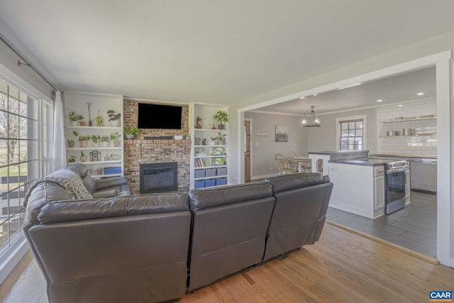 living area with a brick fireplace, crown molding, built in features, wood finished floors, and a notable chandelier