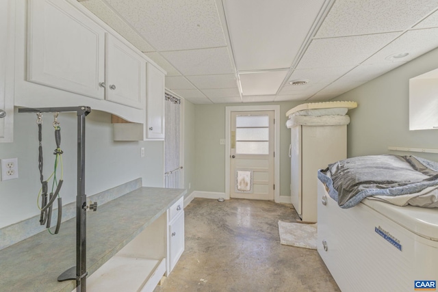 interior space with white cabinetry, concrete floors, light countertops, a paneled ceiling, and baseboards