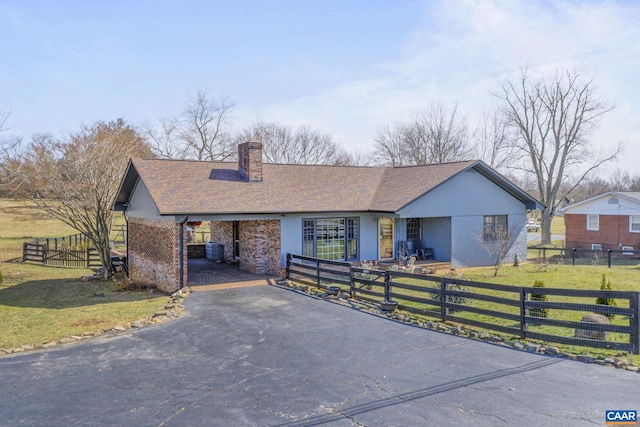 ranch-style house featuring a front yard, a chimney, a fenced front yard, aphalt driveway, and central air condition unit