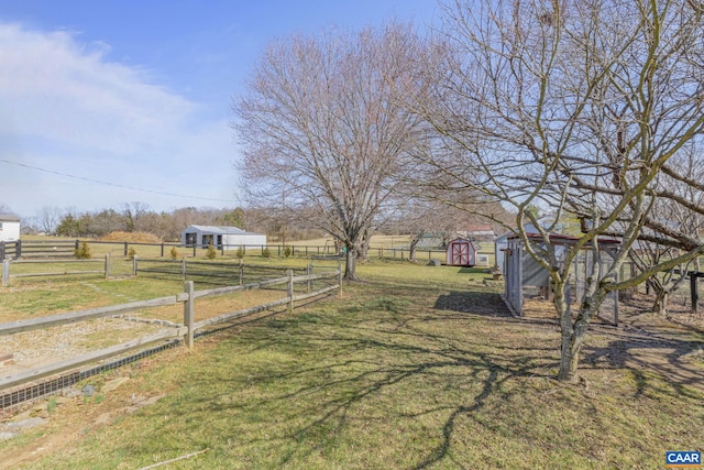 view of yard with a rural view, a shed, an outdoor structure, and fence