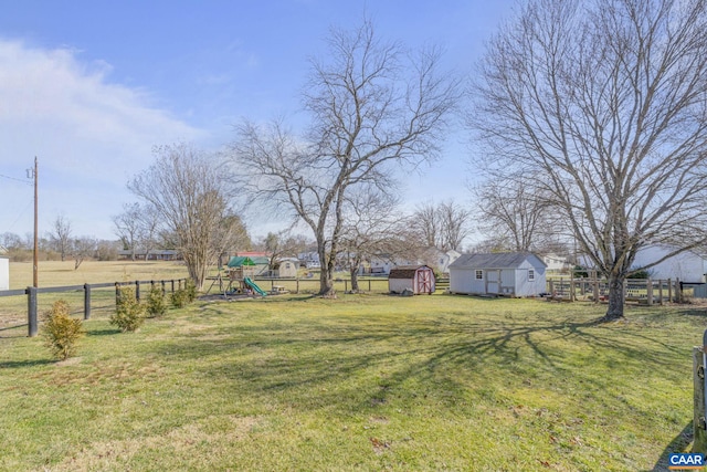 view of yard featuring a storage unit, a playground, an outdoor structure, and fence