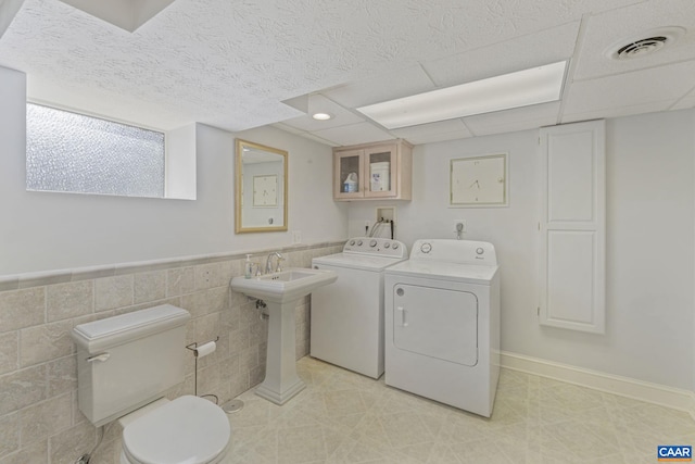 washroom featuring a wainscoted wall, visible vents, laundry area, washer and dryer, and tile walls