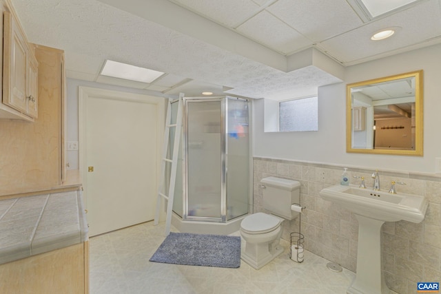 full bath with toilet, a stall shower, a sink, tile walls, and wainscoting