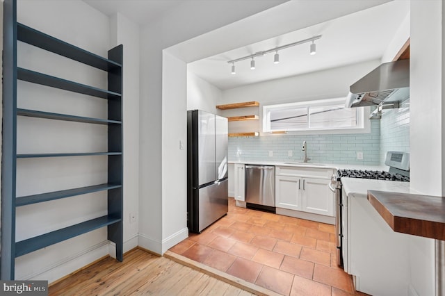 kitchen with open shelves, wall chimney range hood, white cabinets, stainless steel appliances, and a sink