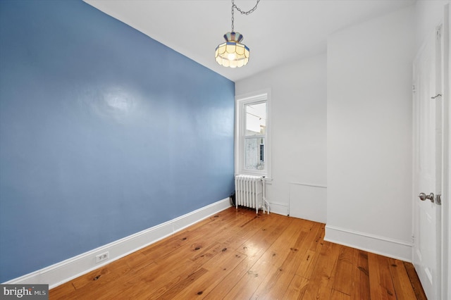 empty room featuring radiator, baseboards, and light wood finished floors