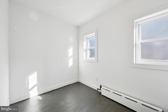 empty room with dark wood-type flooring, baseboards, and a baseboard radiator