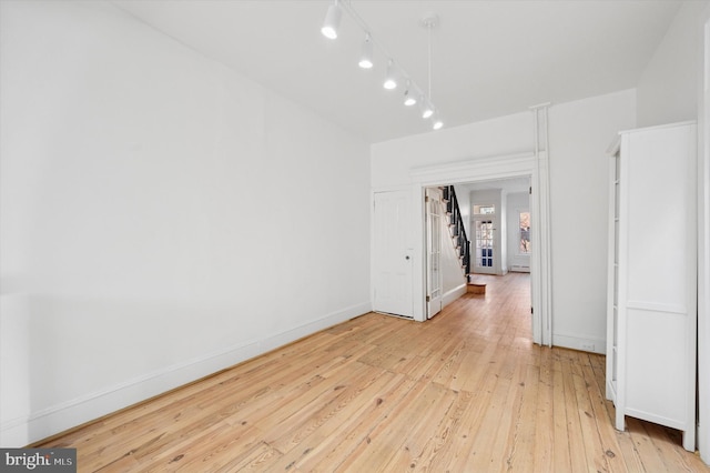 spare room with track lighting, light wood-type flooring, and baseboards