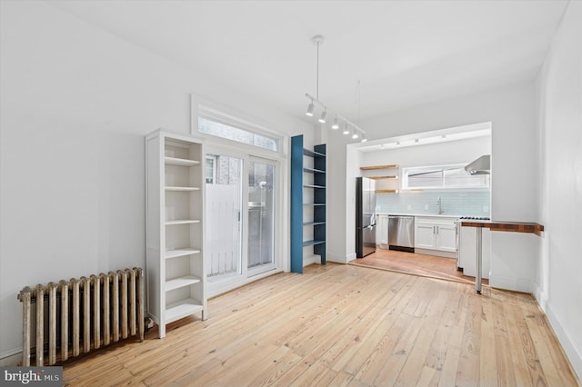 unfurnished dining area featuring light wood finished floors, track lighting, radiator heating unit, and a sink