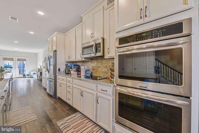 kitchen with dark wood-style floors, visible vents, white cabinets, appliances with stainless steel finishes, and tasteful backsplash