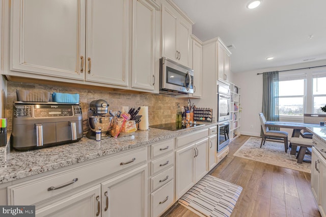 kitchen featuring tasteful backsplash, stainless steel microwave, black electric stovetop, light wood-type flooring, and white cabinetry