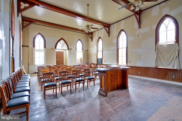 dining space with wood walls, hardwood / wood-style floors, beam ceiling, wainscoting, and a ceiling fan