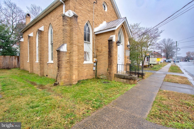 view of property exterior featuring a yard, fence, brick siding, and crawl space