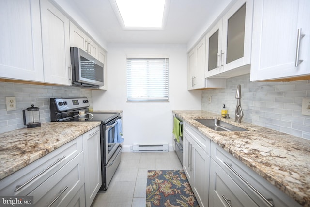 kitchen with glass insert cabinets, a baseboard heating unit, light stone counters, stainless steel appliances, and a sink