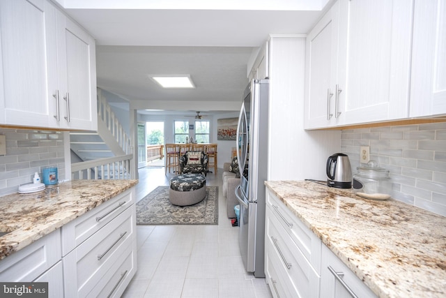 kitchen featuring light stone counters, tasteful backsplash, white cabinets, and freestanding refrigerator