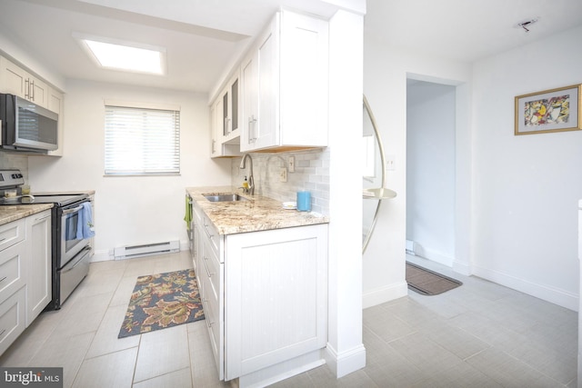 kitchen with light stone countertops, a baseboard radiator, a sink, appliances with stainless steel finishes, and backsplash