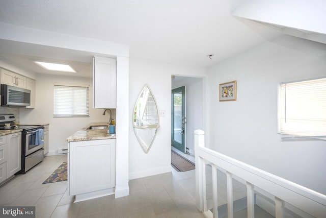 kitchen featuring a sink, baseboards, light stone counters, stainless steel appliances, and a baseboard radiator