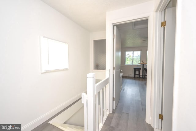 corridor with baseboards, an upstairs landing, baseboard heating, and wood finished floors