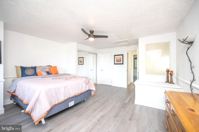 bedroom with a ceiling fan, attic access, light wood-style floors, a closet, and a textured ceiling