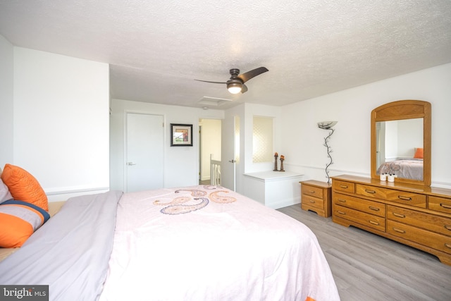 bedroom with light wood-style flooring, a textured ceiling, attic access, and ceiling fan