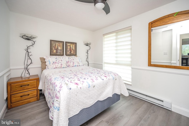 bedroom featuring a baseboard heating unit, wood finished floors, and ceiling fan