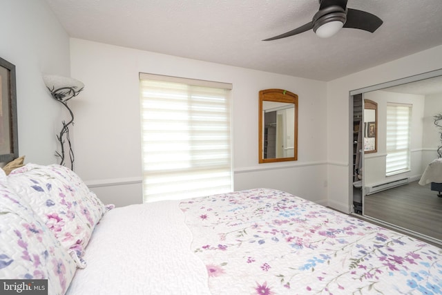 bedroom with baseboard heating, a textured ceiling, a ceiling fan, and wood finished floors