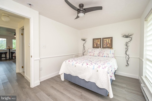 bedroom featuring wood finished floors, baseboard heating, and a textured ceiling