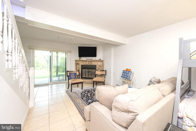 living area featuring a stone fireplace, light tile patterned floors, baseboards, and stairs