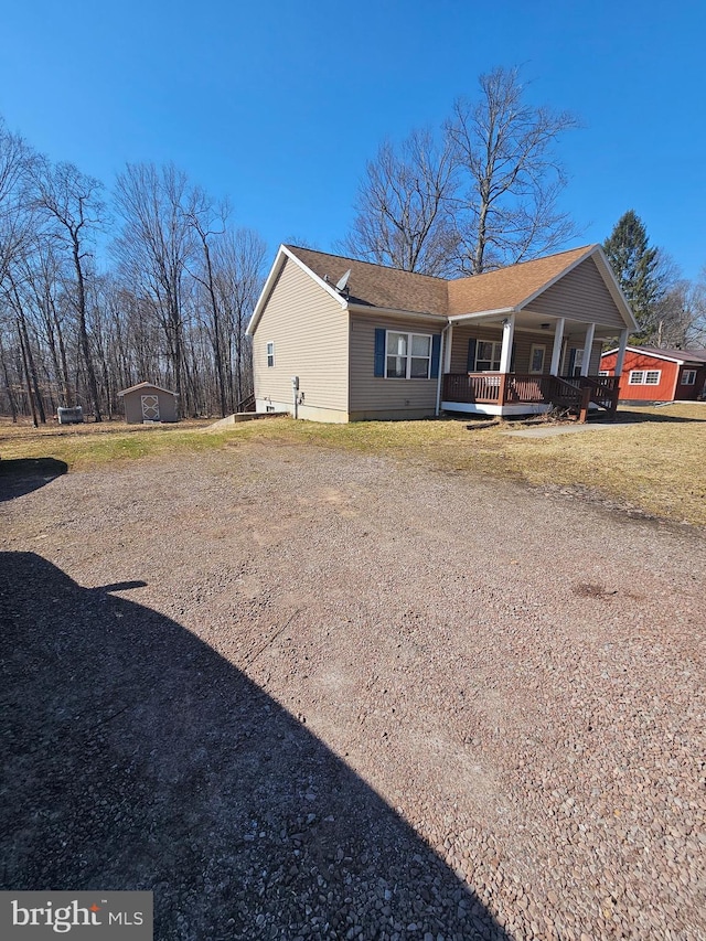 view of property exterior featuring an outbuilding, a shed, a porch, a yard, and dirt driveway