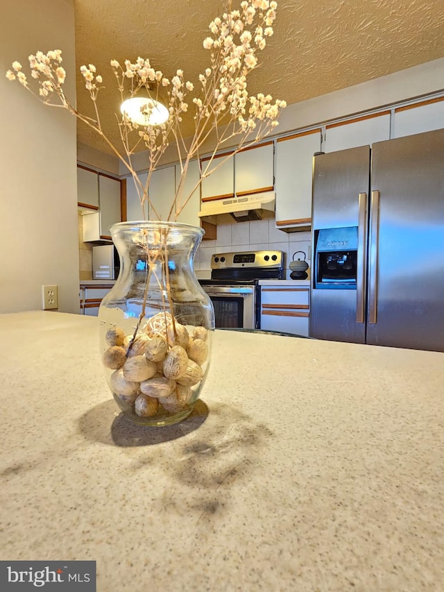 kitchen featuring under cabinet range hood, stainless steel appliances, backsplash, and a textured ceiling