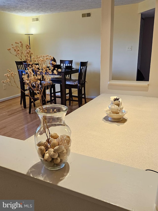 dining room featuring visible vents, a textured ceiling, baseboards, and wood finished floors