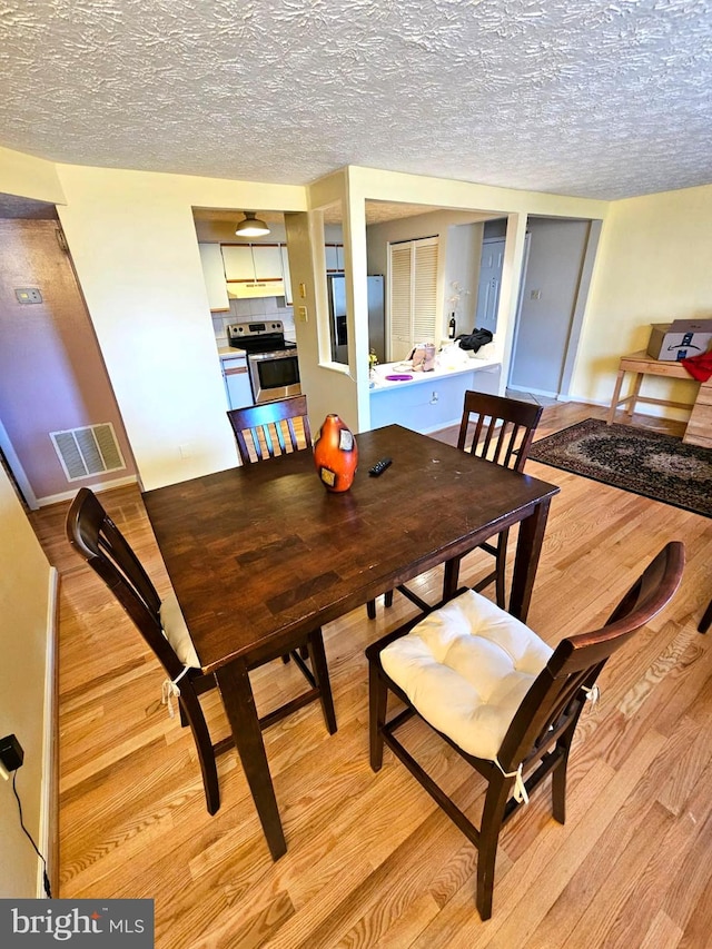 dining room featuring visible vents, a textured ceiling, and light wood-style flooring