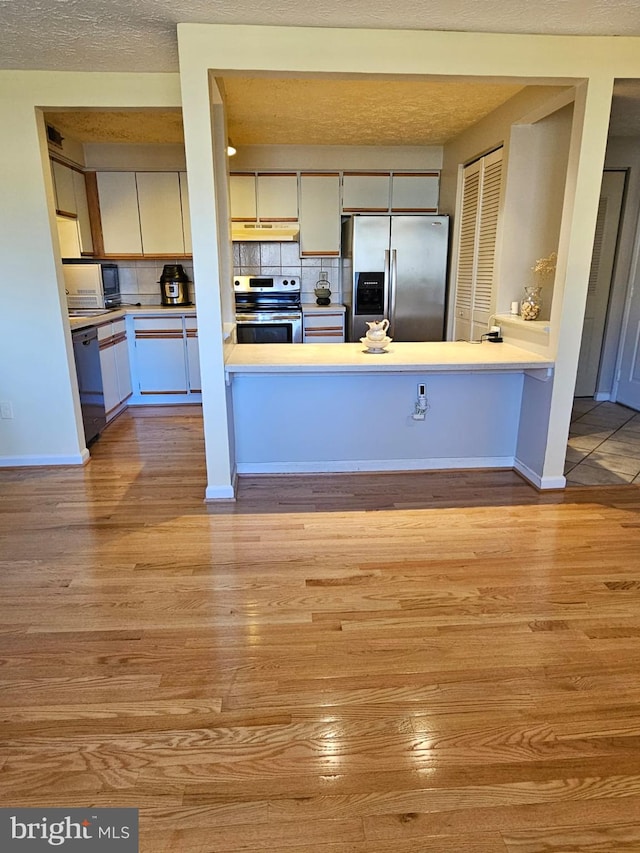 kitchen with wood finished floors, light countertops, under cabinet range hood, appliances with stainless steel finishes, and tasteful backsplash