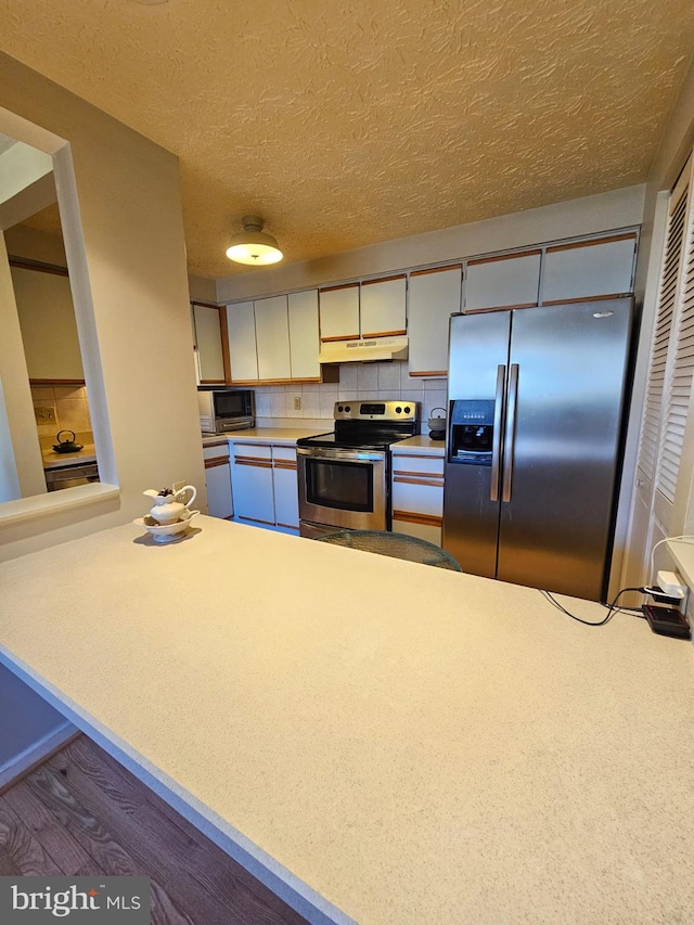 kitchen with a textured ceiling, light countertops, under cabinet range hood, appliances with stainless steel finishes, and tasteful backsplash