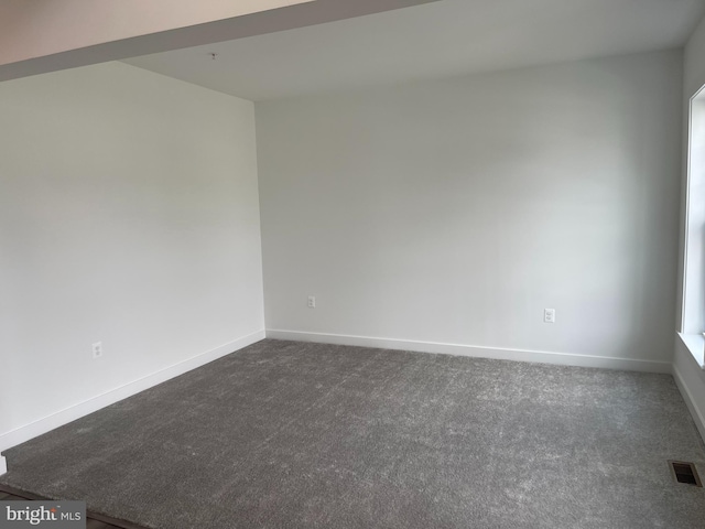 unfurnished room with baseboards, visible vents, and dark colored carpet