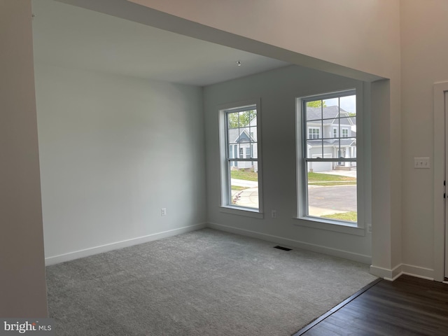 unfurnished room featuring dark colored carpet, baseboards, and dark wood-style floors