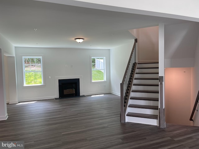 unfurnished living room with a fireplace with flush hearth, stairs, baseboards, and dark wood-style flooring