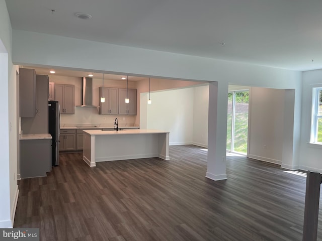 kitchen featuring gray cabinetry, wall chimney range hood, light countertops, freestanding refrigerator, and a sink