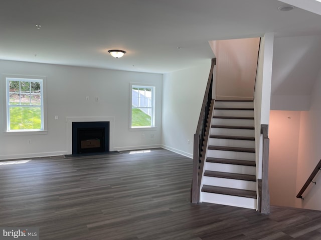 unfurnished living room with dark wood-style floors, stairway, baseboards, and a fireplace with flush hearth