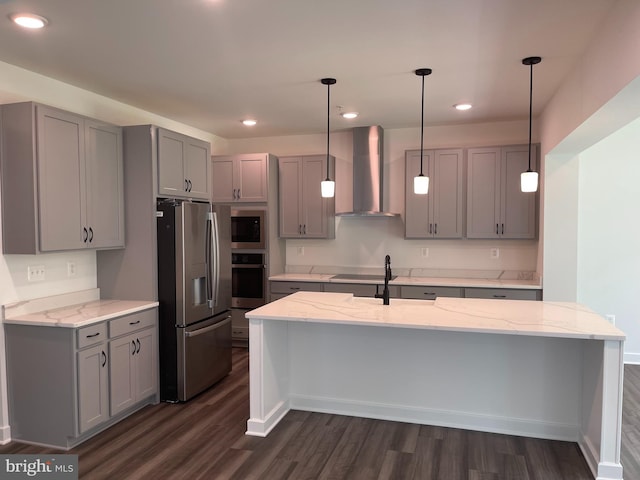 kitchen with gray cabinetry, dark wood-style floors, appliances with stainless steel finishes, wall chimney exhaust hood, and light stone countertops