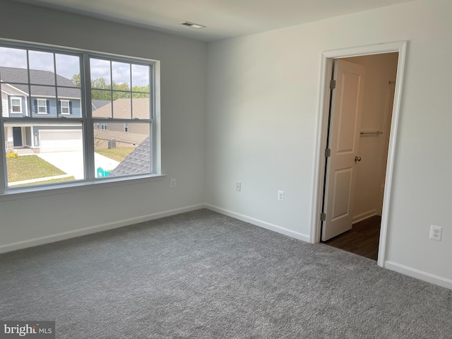 empty room featuring baseboards, visible vents, and dark carpet