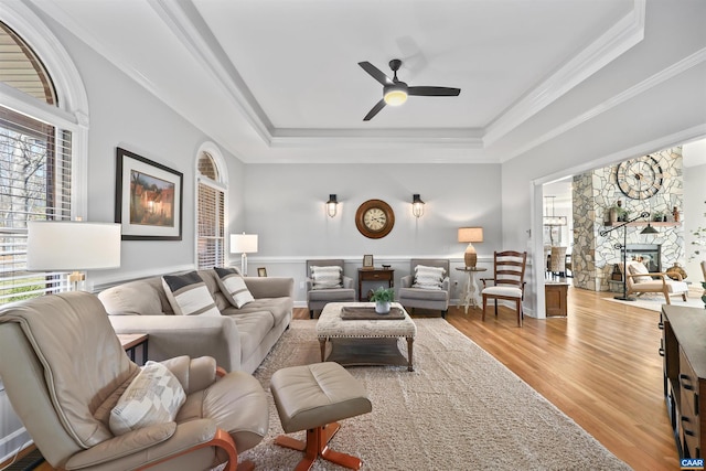 living area featuring a raised ceiling, crown molding, wood finished floors, and ceiling fan