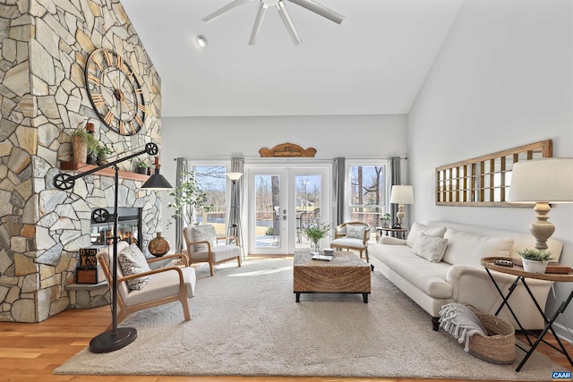 living area featuring a stone fireplace, high vaulted ceiling, wood finished floors, and ceiling fan